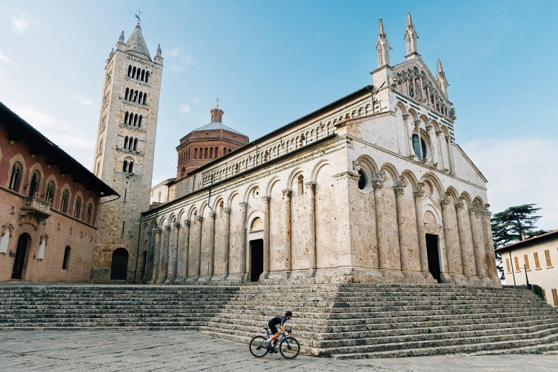 Cyclist passing the Romanesque cathedral of Massa Marittima in Maremma, Tuscany