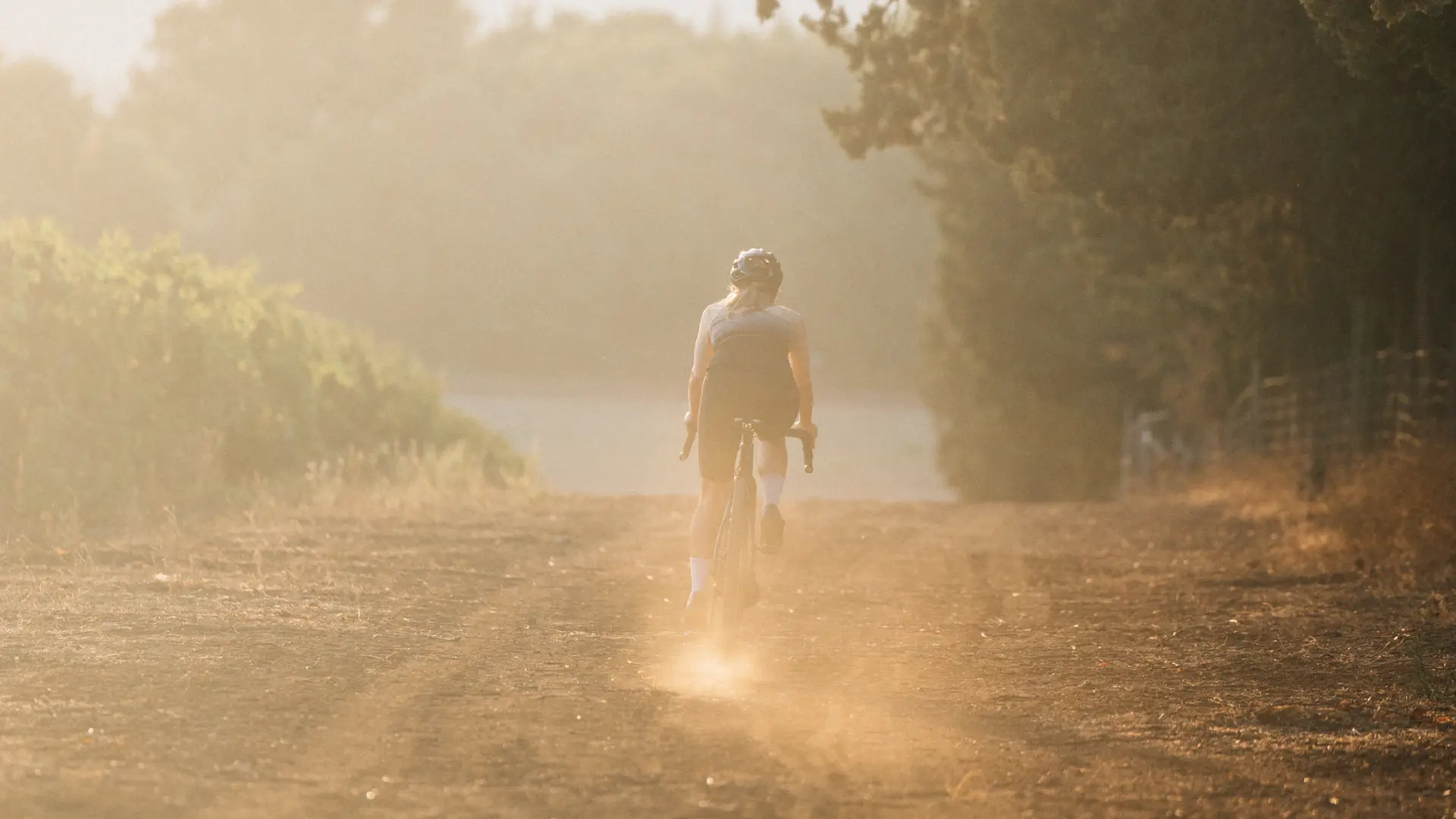 Una ciclista che scompare nella polvere su strada bianca all'alba